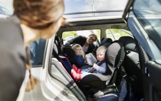 Two womens talking to each other with kids in car.